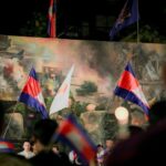 People holding cambodian flags in front of a mural.