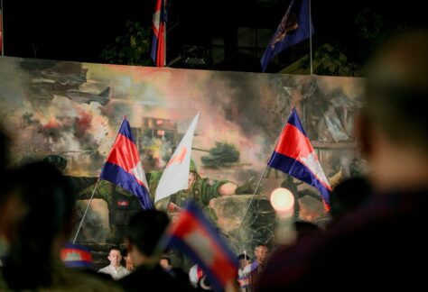 People holding cambodian flags in front of a mural.