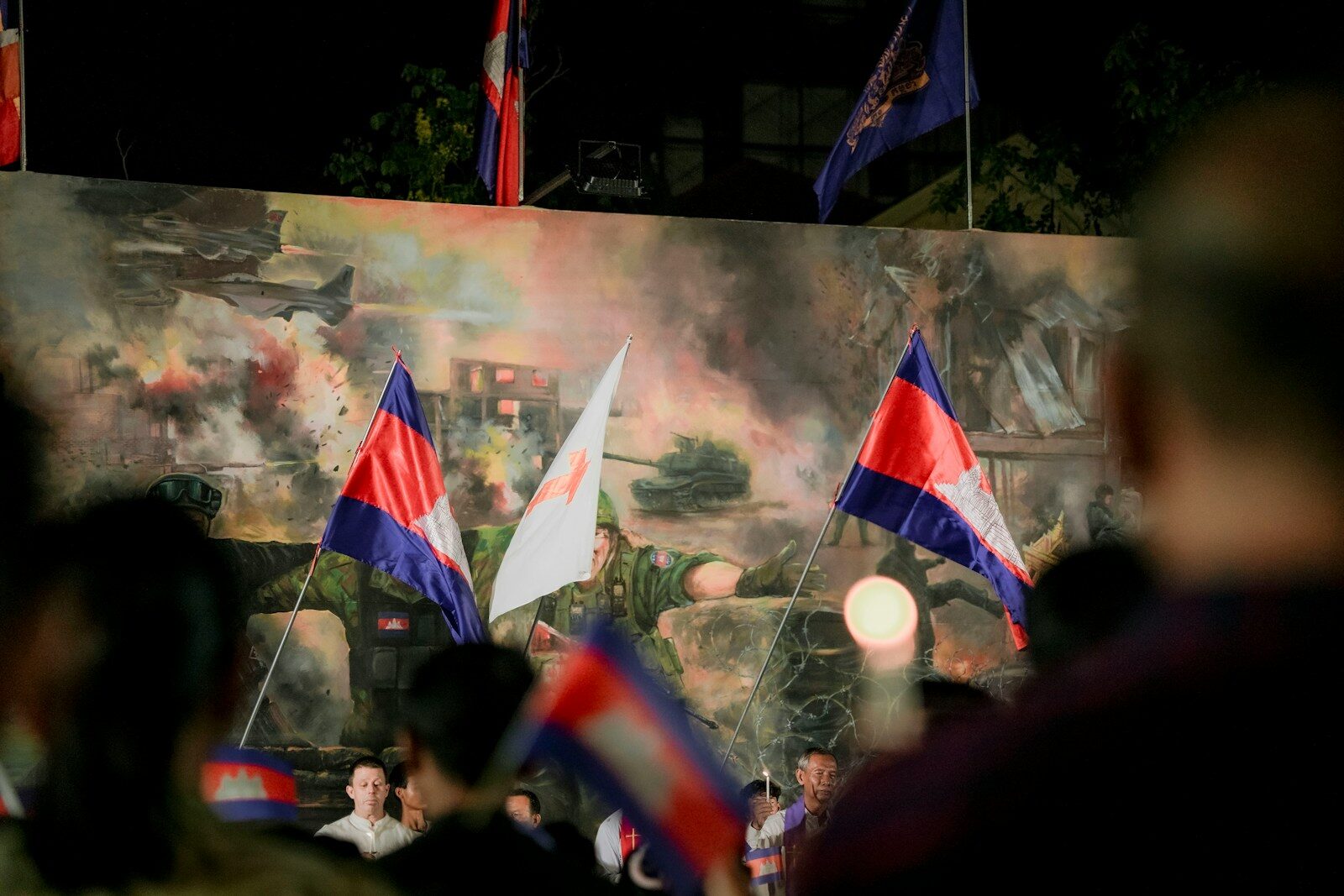 People holding cambodian flags in front of a mural.